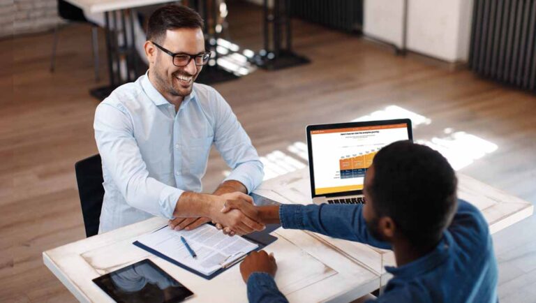 Data Strategy: Internally Hiring vs Outsourcing–Two businessmen, Caucasian and African American, in an office setting, shaking hands in agreement on a data strategy plan to hire our outsource their data team. A laptop is open with Mutually Humans website